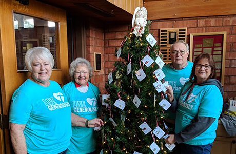 four people standing around christmas tree hung with more than 20 name labels