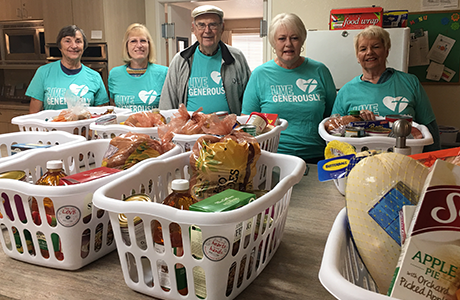 five people standing behind eight baskets full of thanksgiving food items